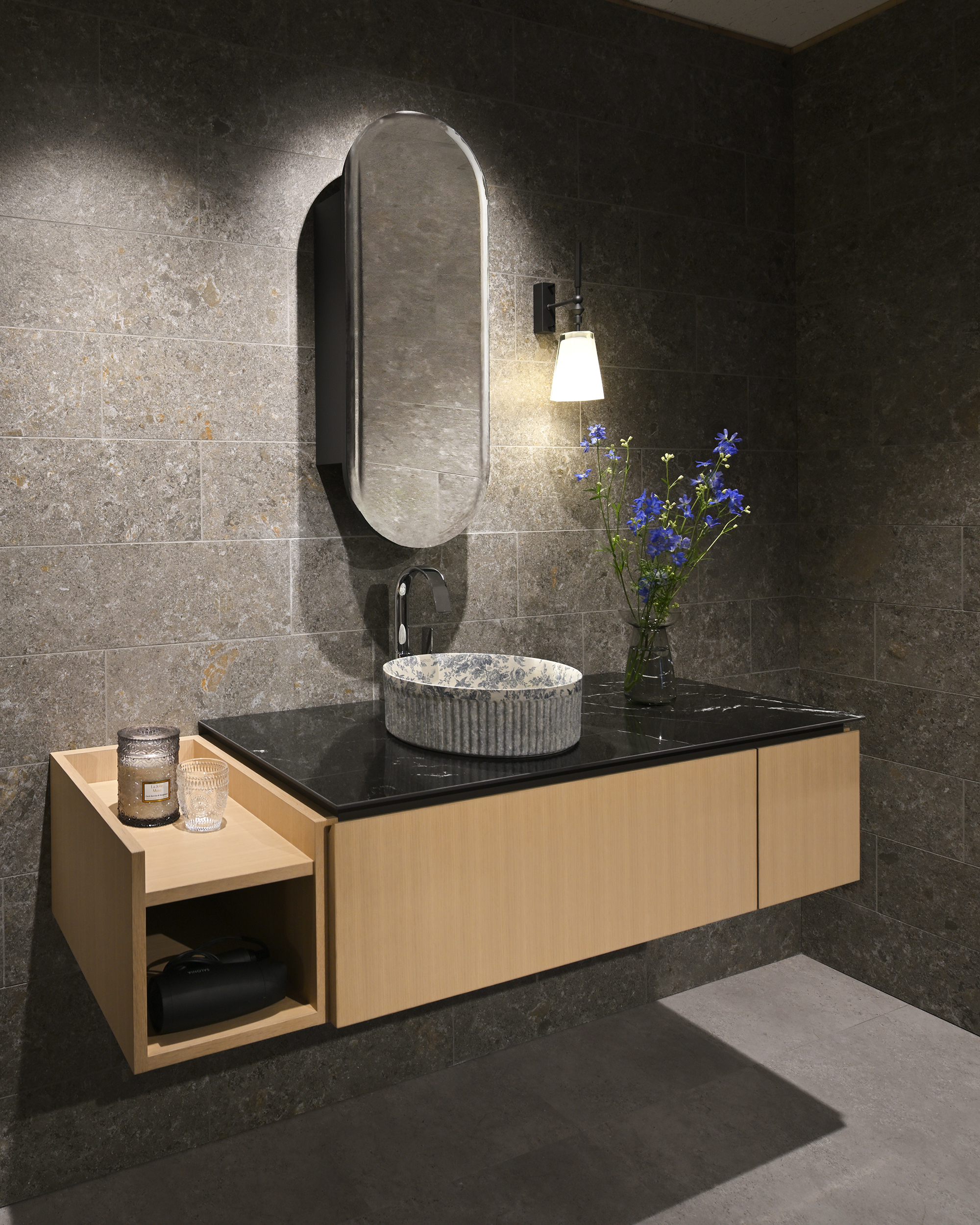 石目の壁とブラックのカウンター、木のキャビネットに合わせたBATHCO「WADI」。